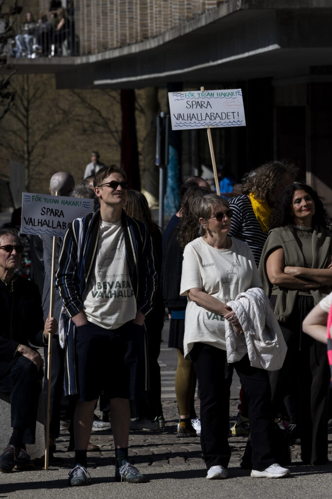 Filip Laurits iklädd en t-shirt med texten "bevara Valhalla" på en demonstration. Runt honom står människor med skyltar, på vilka det står "spara Valhallabadet!".