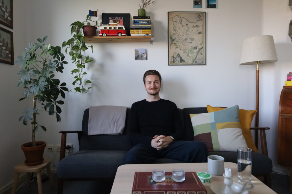 Isak Wreland, iklädd en svart tröja, sitter i en soffa med färgglada kuddar.