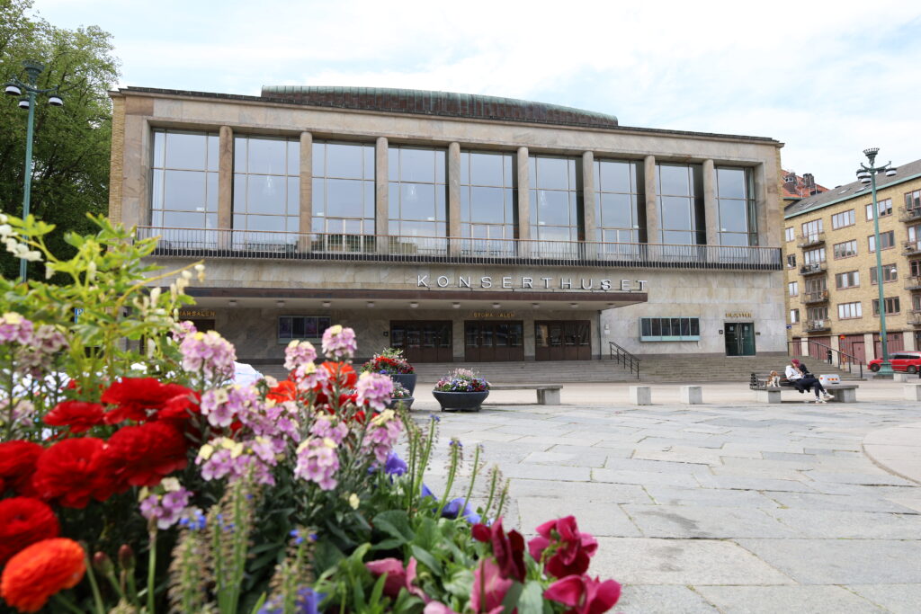 I förgrunden rosa och röda blommor. I bakgrunden Konserthuset med nio stora fönster ovanför entrén.