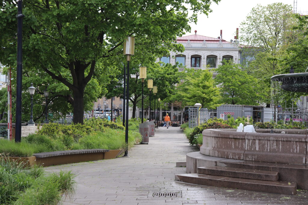 Bild av Brunnsparken i Göteborg. Där man skymtar en fontän, gatulampor, träd och planteringar.