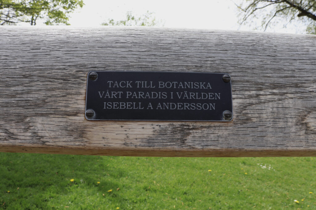 Närbild på en personlig skylt på en bänk i Botaniska trädgården. Texten lyder: "Tack till Botaniska, vårt paradis i världen, Isabell A Andersson".