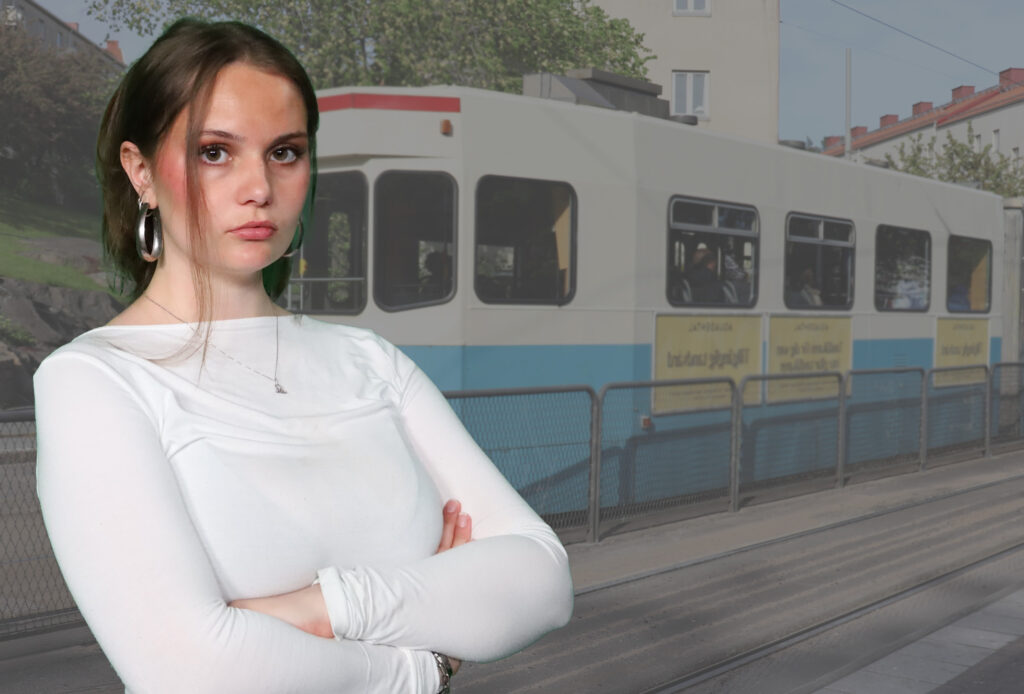 Maja Matsdotter, iklädd en vit tröja, tittar in i kameran med korsade armar. I bakgrunden åker en spårvagn förbi.
