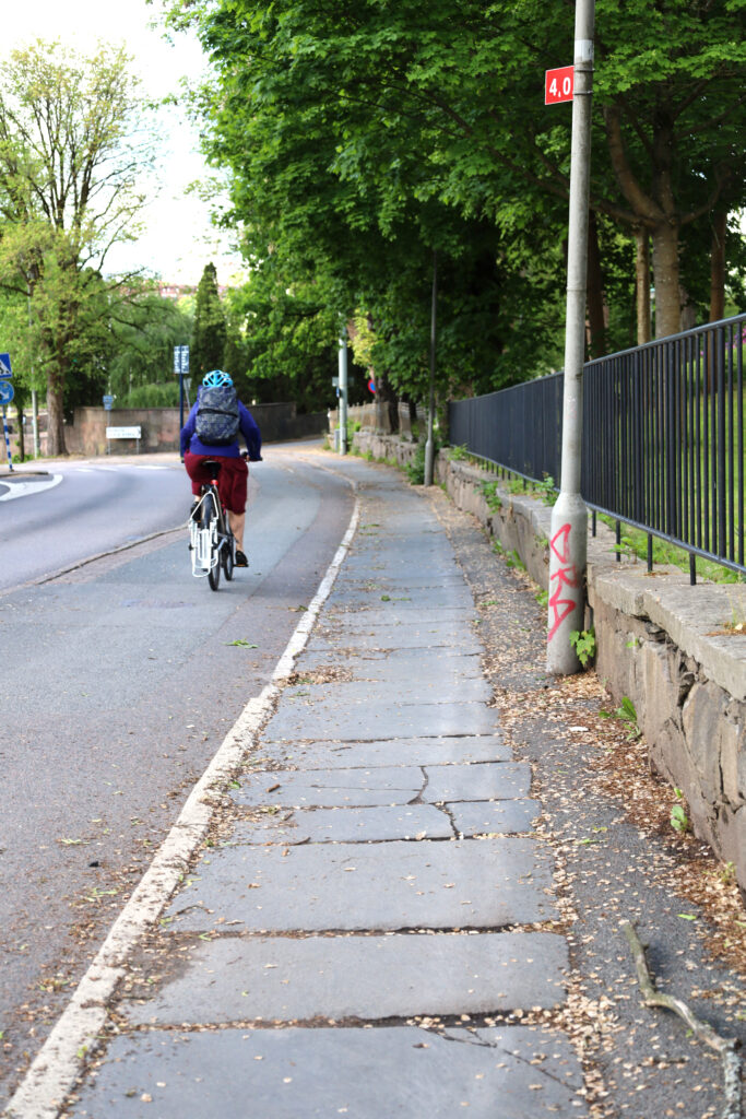 En cyklist, iklädd röda byxor och en lila jacka, på en cykelbana.