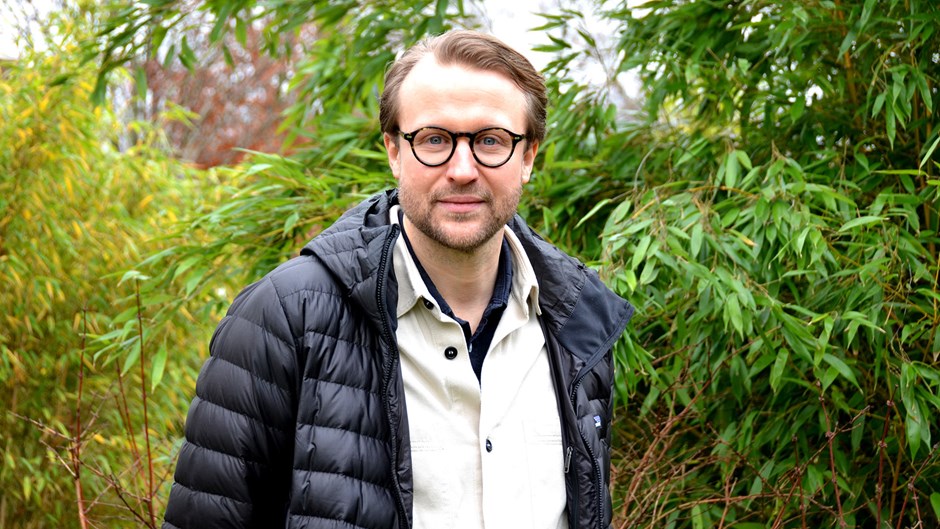 Johan Rehngren, iklädd svart dunjacka, tittar in i kameran. Bakom honom gröna träd.