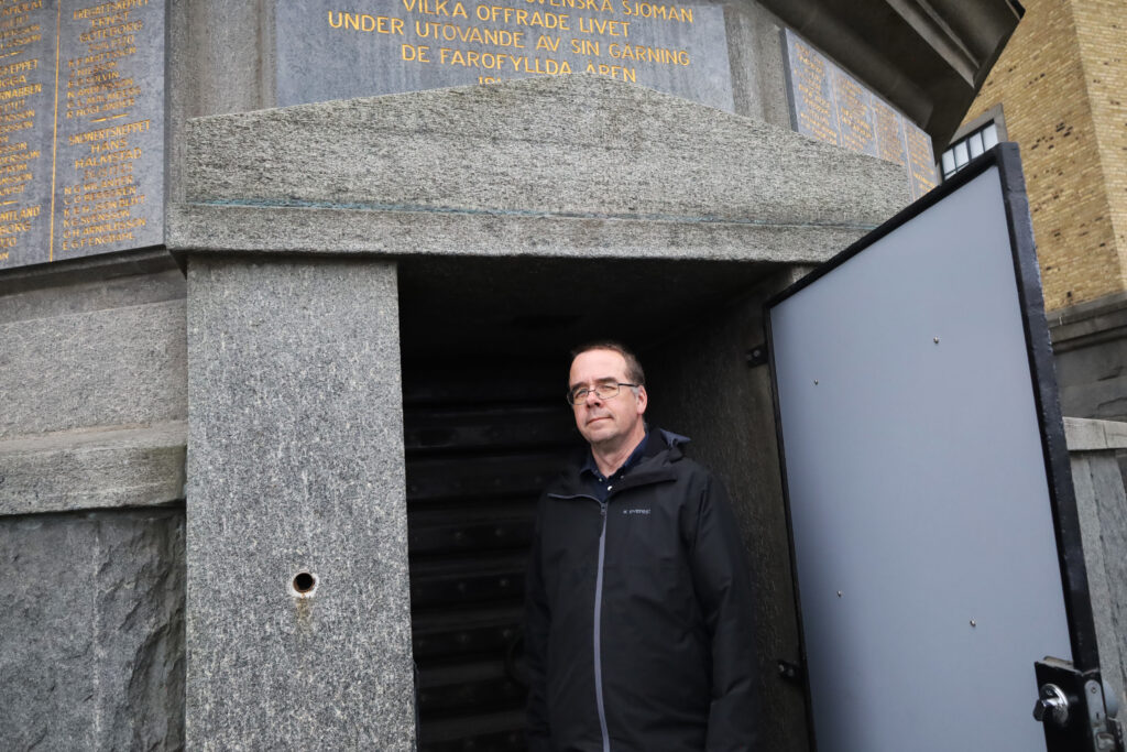 Karl Hellervik, iklädd svart jacka och med glasögon, står i dörröppningen till stentornet med Sjömanshustrun högst upp.