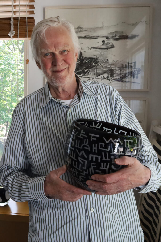 Olle Anderson, iklädd en blå- och vitrandig skjorta, håller i en svart skål med vita symboler.
