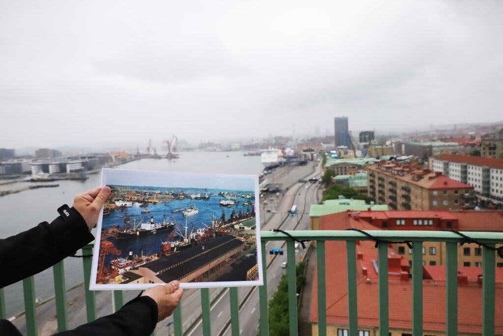 Karl Hellervik håller upp ett foto som visar Göteborgs hamn innan tornet och Sjömanshustrun byggdes. Fotot visar många båtar i Göta älv och mängder av kranar i hamnen. 