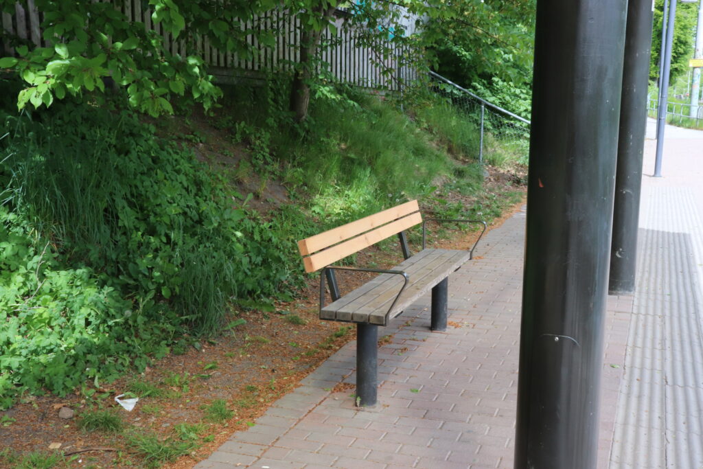 En parkbänk i trä på Botaniska Trädgårdens spårvagnsstation.